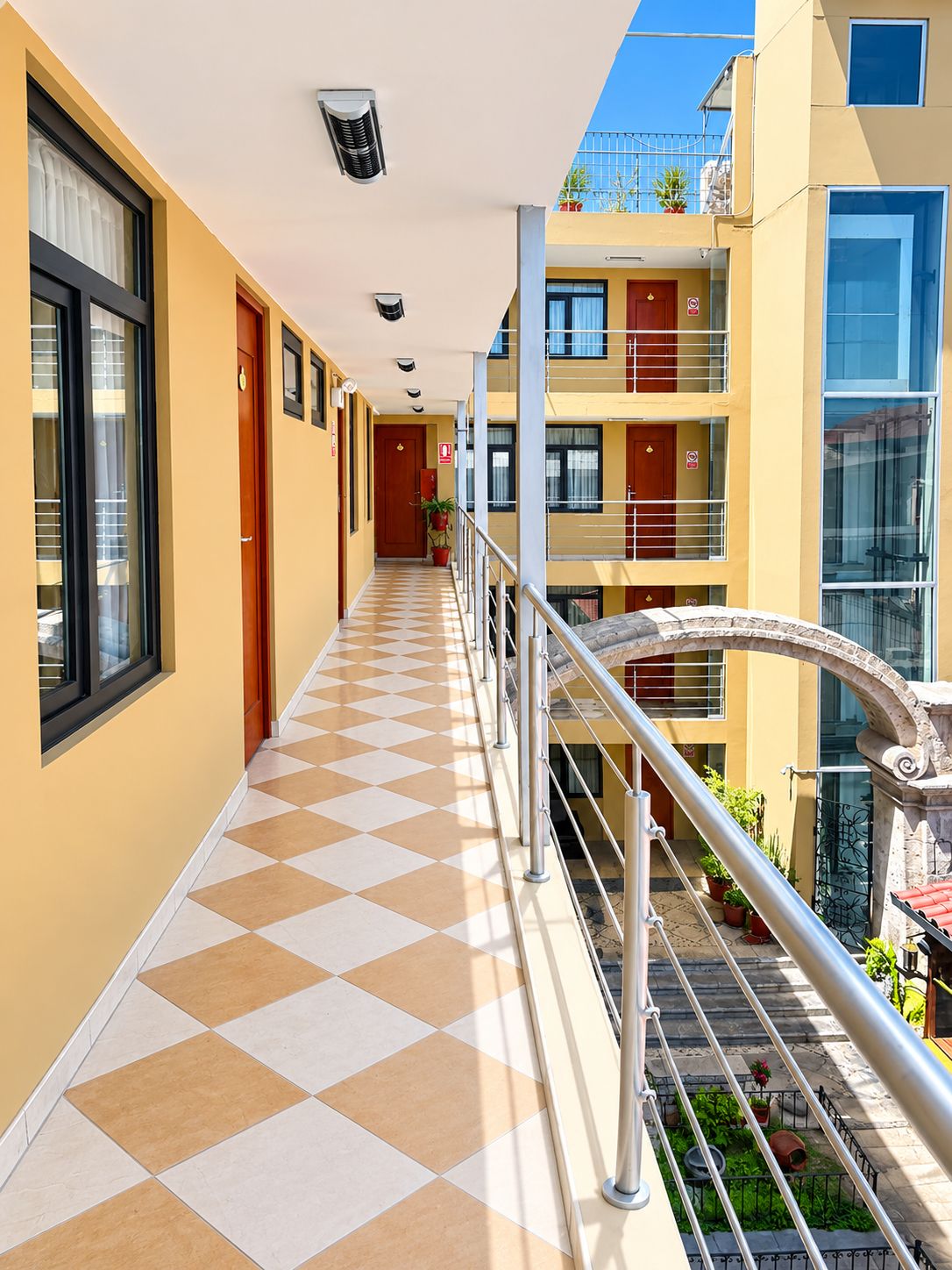 A corridor with a checkered floor, a metal railing, and a view of a building with multiple balconies and windows.