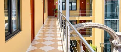 A corridor with a checkered floor, a metal railing, and a view of a building with multiple balconies and windows.