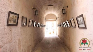 A corridor with framed pictures on the walls, leading to a bright exit. - Hotel Santa Rosa (Arequipa)