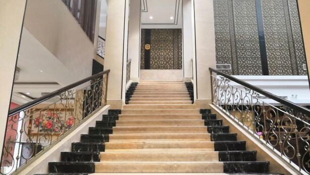 Una imponente escalera con peldaños en blanco y negro, barandillas de metal ornamentadas y un revestimiento con motivos en la parte superior.