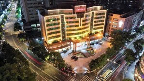 Un hotel de varios pisos con un patio central, rodeado por una concurrida calle urbana.