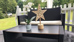 Een rieten bijzettafeltje met een sterosdecoratie, een plant in een pot en een kussen op een terras.