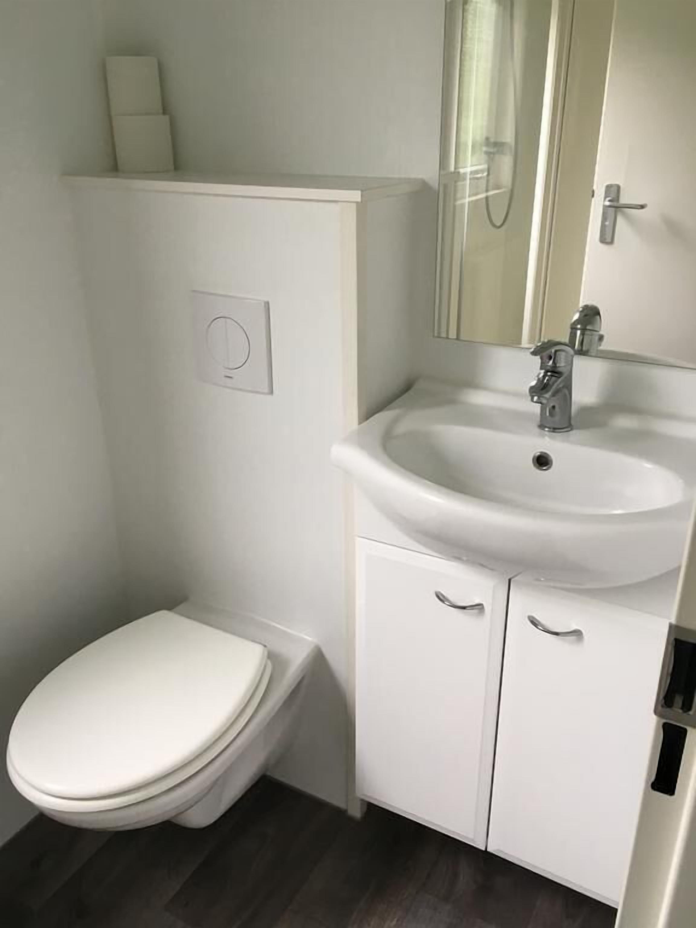 Ein kleines, modernes Badezimmer mit Toilette, Waschbecken und Spiegel.