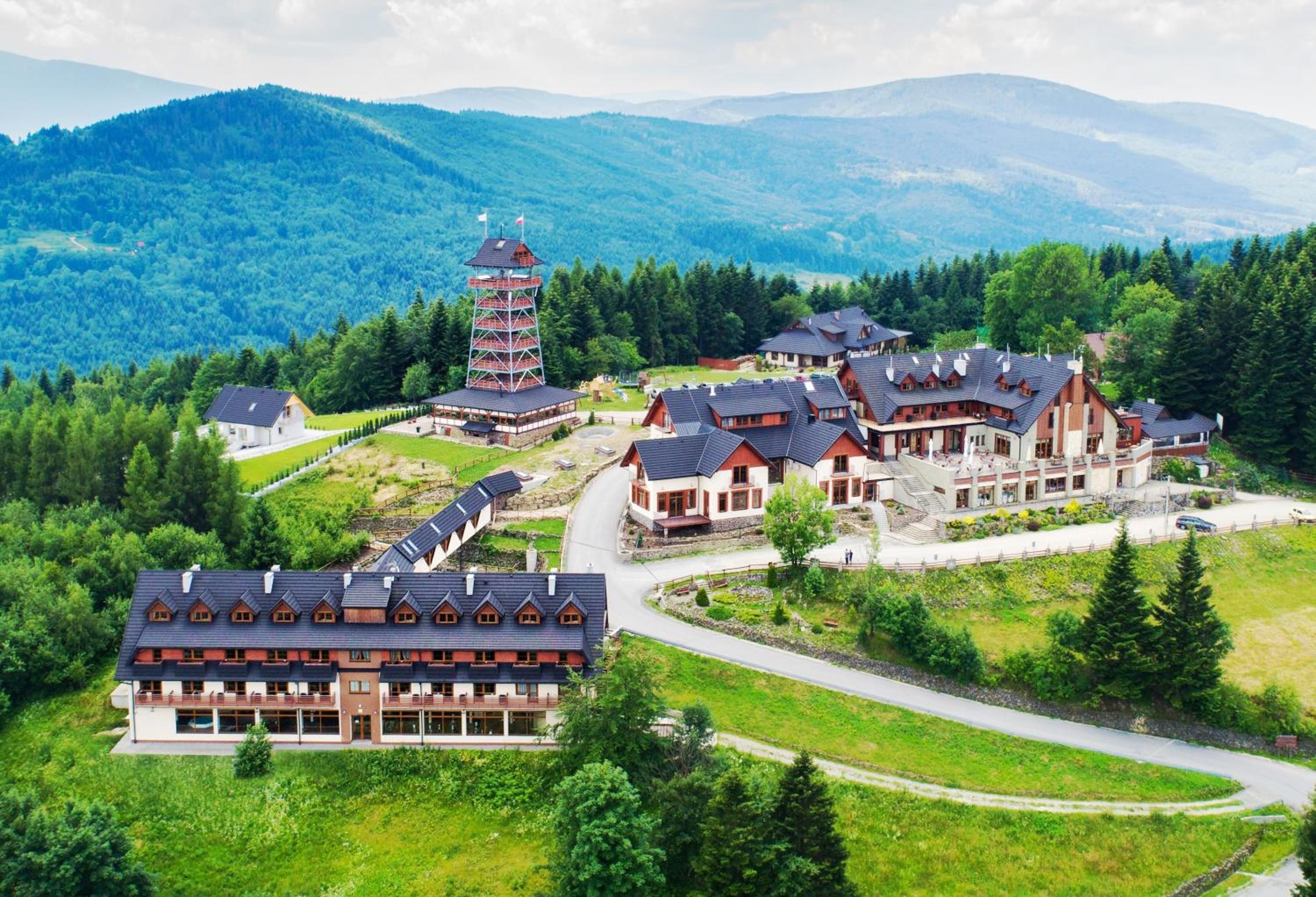 Een resort met meerdere chalethuizen, een centraal torentje en een bergachtige achtergrond.