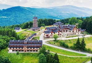A resort with multiple chalet-style buildings, a central tower, and a mountainous backdrop. - Hotel Beskidzki Raj Medical Spa (Stryszawa)