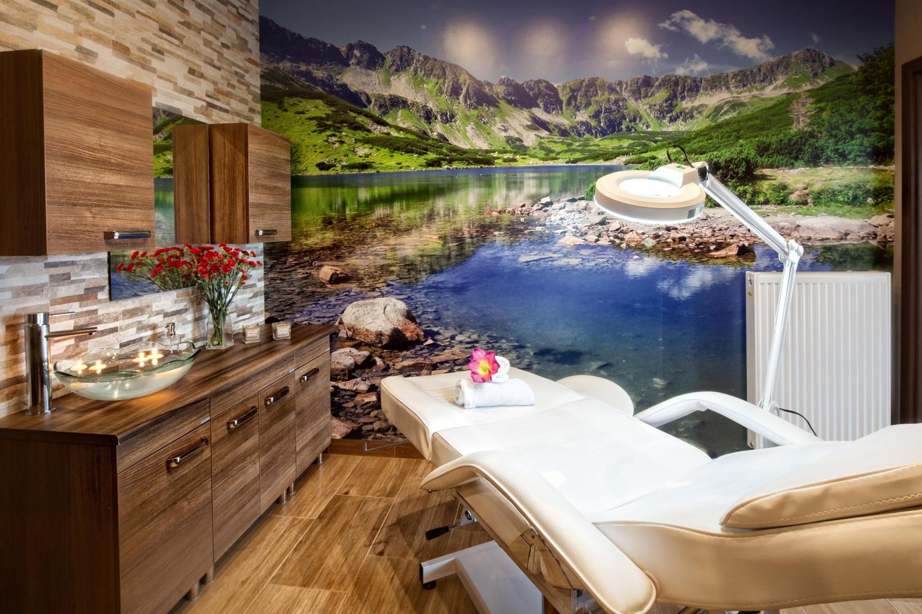 Une salle de spa avec vue sur un lac de montagne, un meuble en bois, un lavabo en verre et une table de massage.