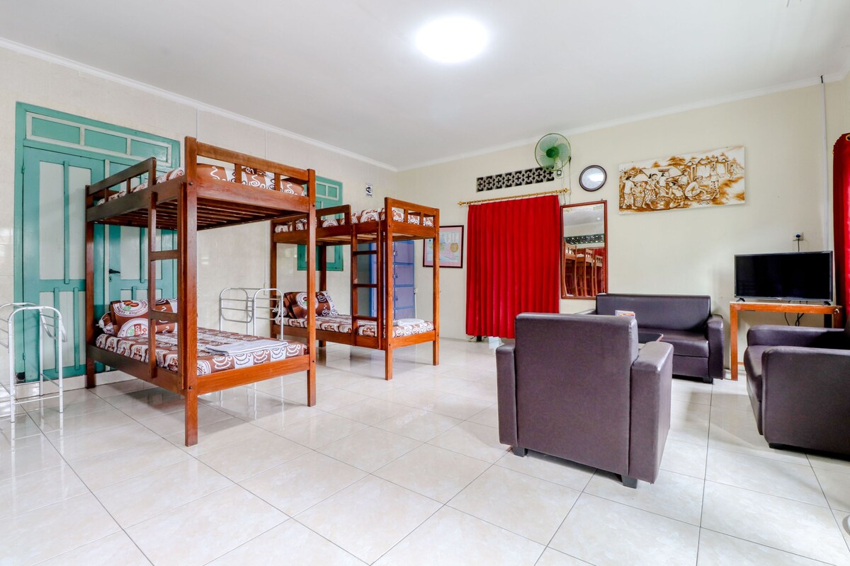 Um quarto com duas beliches de madeira, um sofá cinza, uma televisão e uma cortina vermelha.
