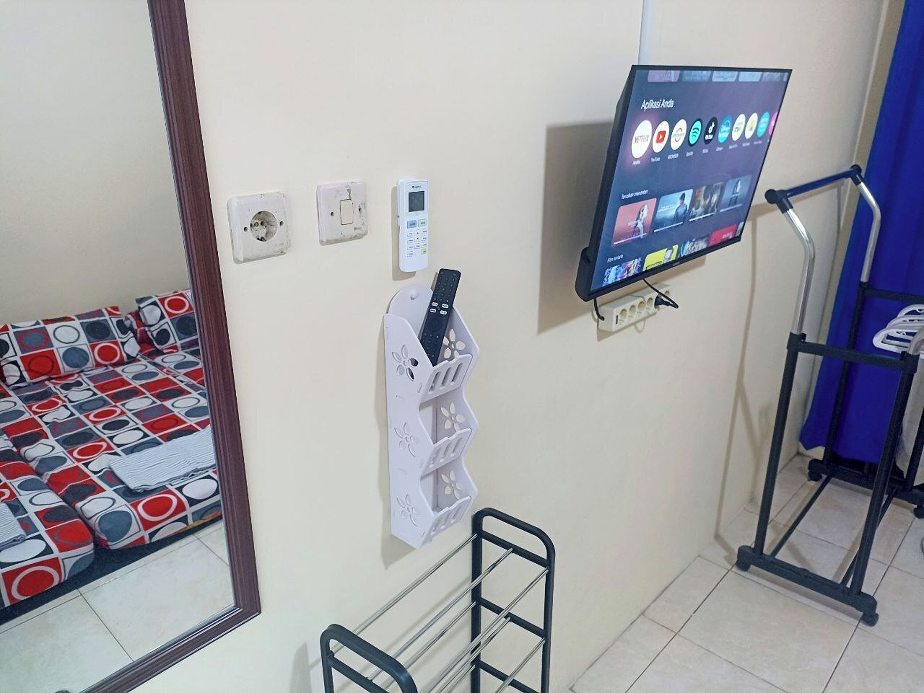 Una habitación con cama, televisión montada en la pared, cinta de correr y espejo.