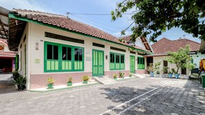 A building with green doors and windows, a tiled roof, and a paved walkway. - Bahagia Sederhana Home Stay - Hostel (Bantul)