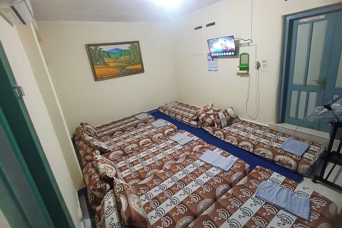 Un alojamiento pequeño y de una sola habitación, con una cama, un televisor en la pared, una puerta y una ventana.