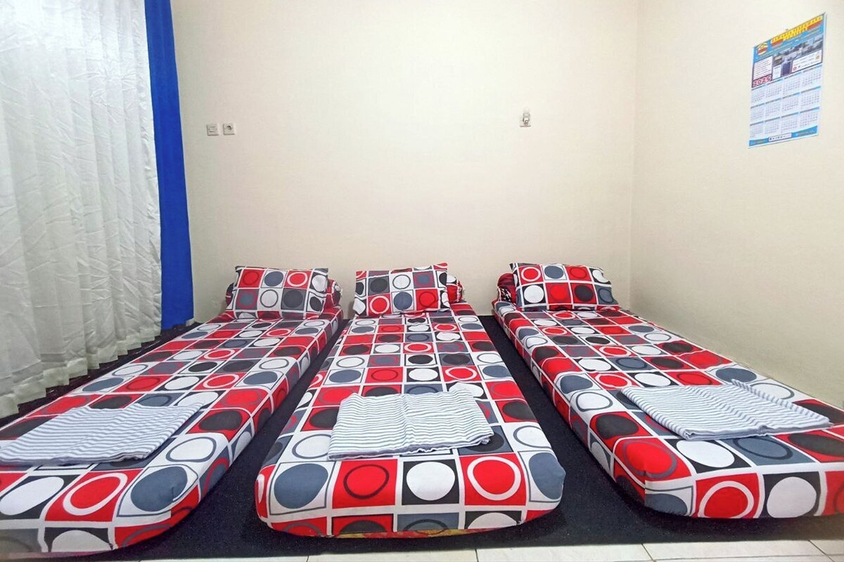 Ein Zimmer mit drei Einzelbetten, jedes mit einer Bettdecke im roten, weißen und schwarzen Muster.