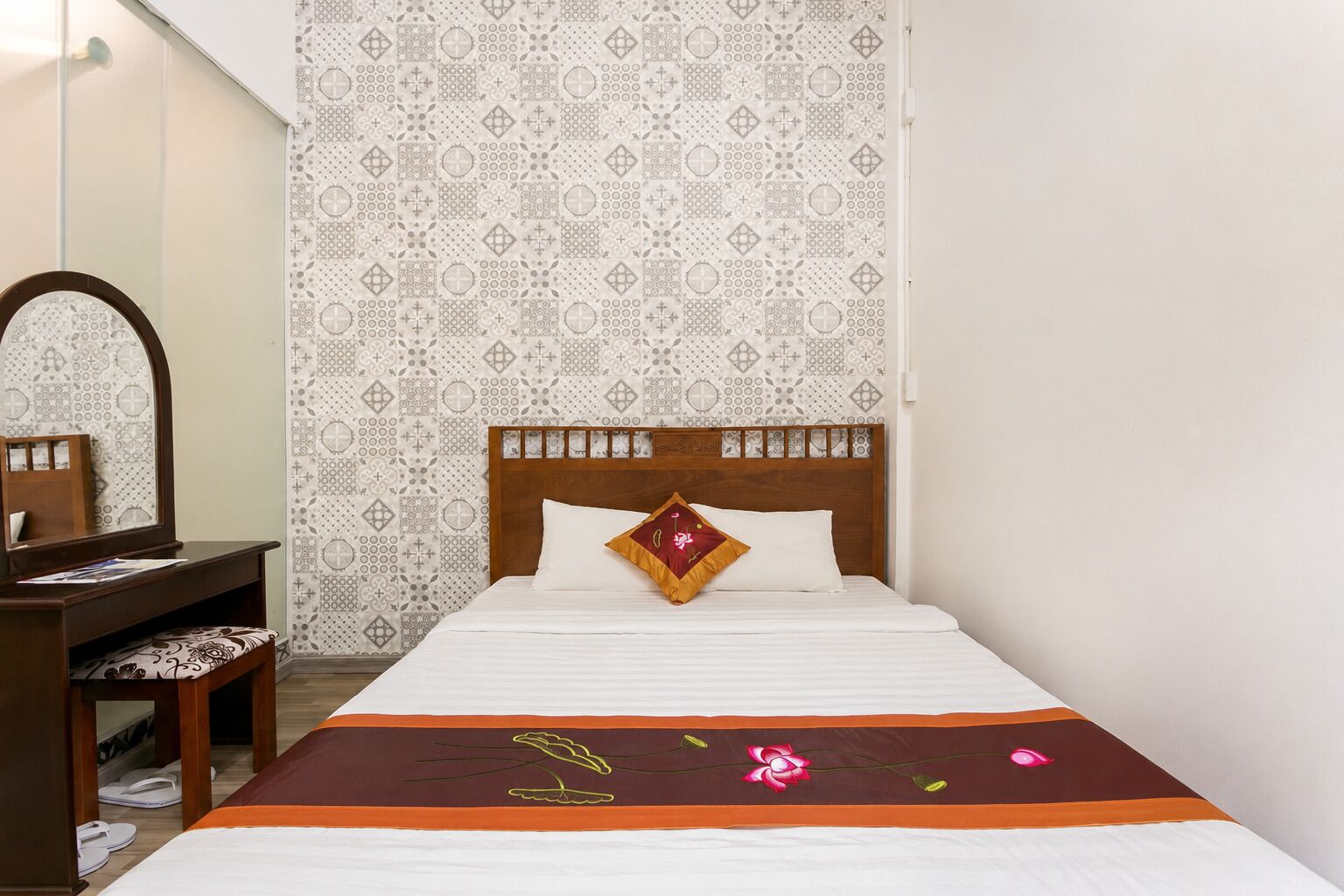 A bedroom with a bed, a wooden nightstand, a mirror, and patterned wallpaper.