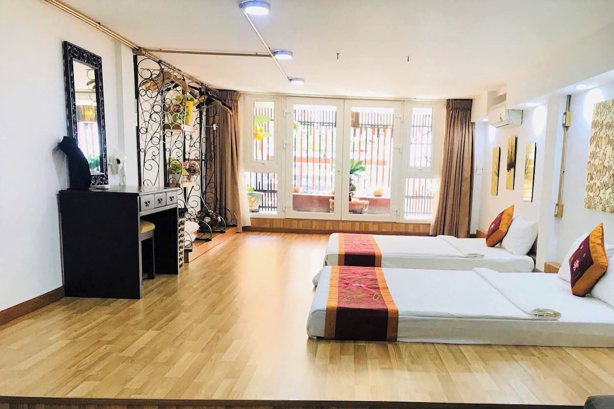 Habitación de hotel con dos camas, un escritorio, un aparador y un ventanal con cortinas.