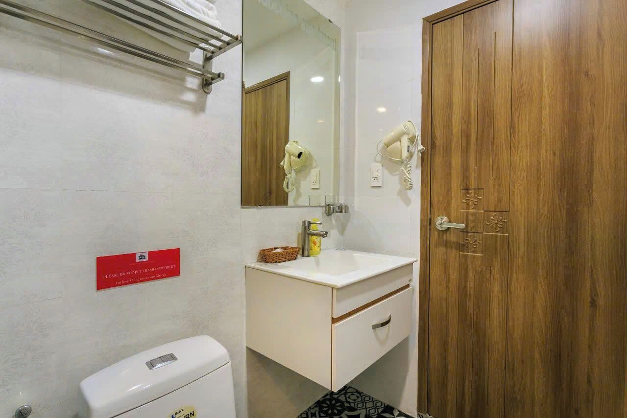 Een badkamer met een wit wastafelmeubel, een spiegel, een houten deur en een rood bord aan de muur.