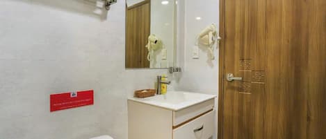 Un baño con un lavamanos blanco, un espejo, una puerta de madera y un letrero rojo en la pared.