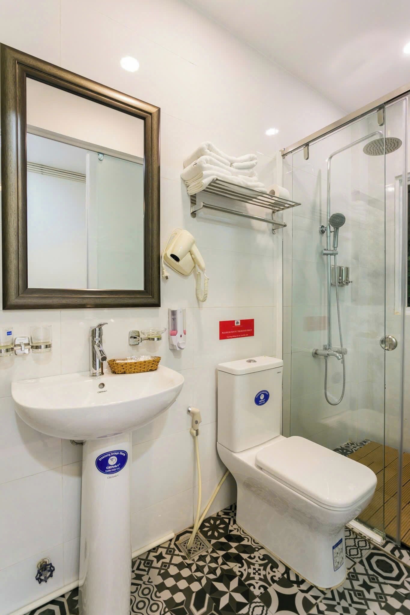 A bathroom with a sink, mirror, hairdryer, and a glass-enclosed shower.
