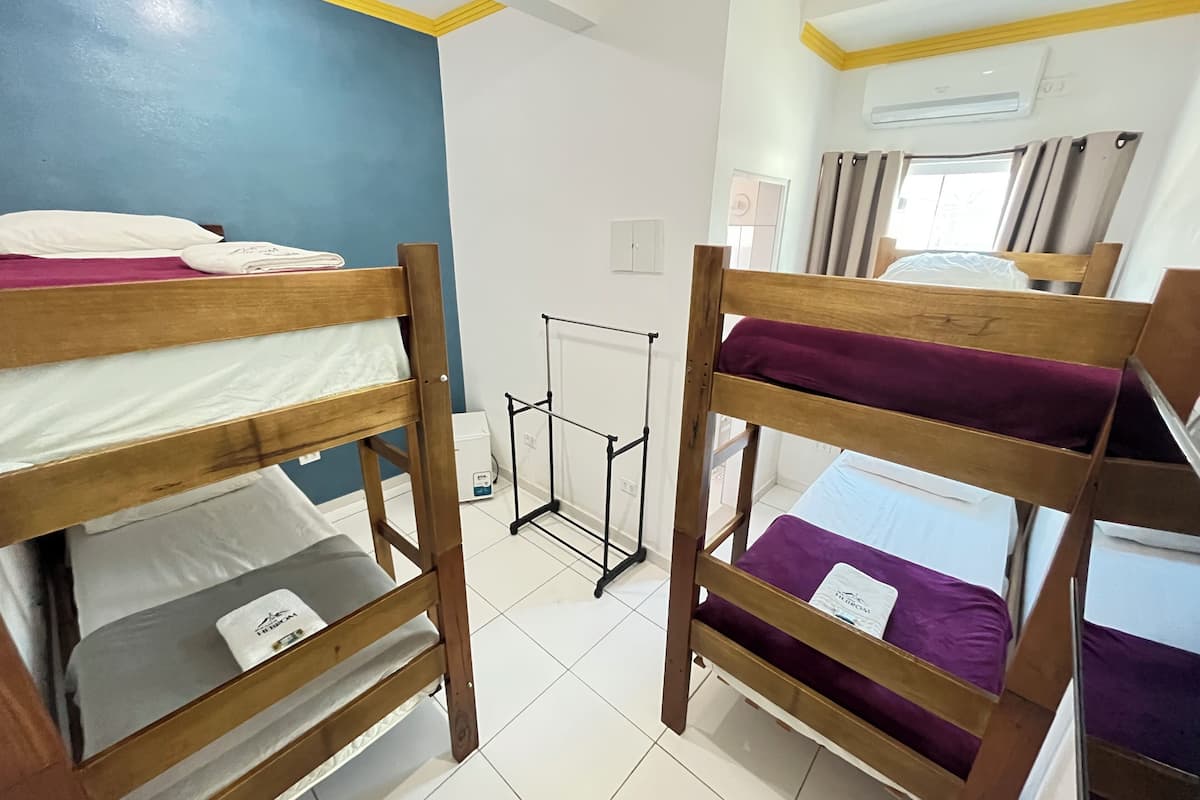 A dormitory room with bunk beds, a radiator, and a window with curtains.