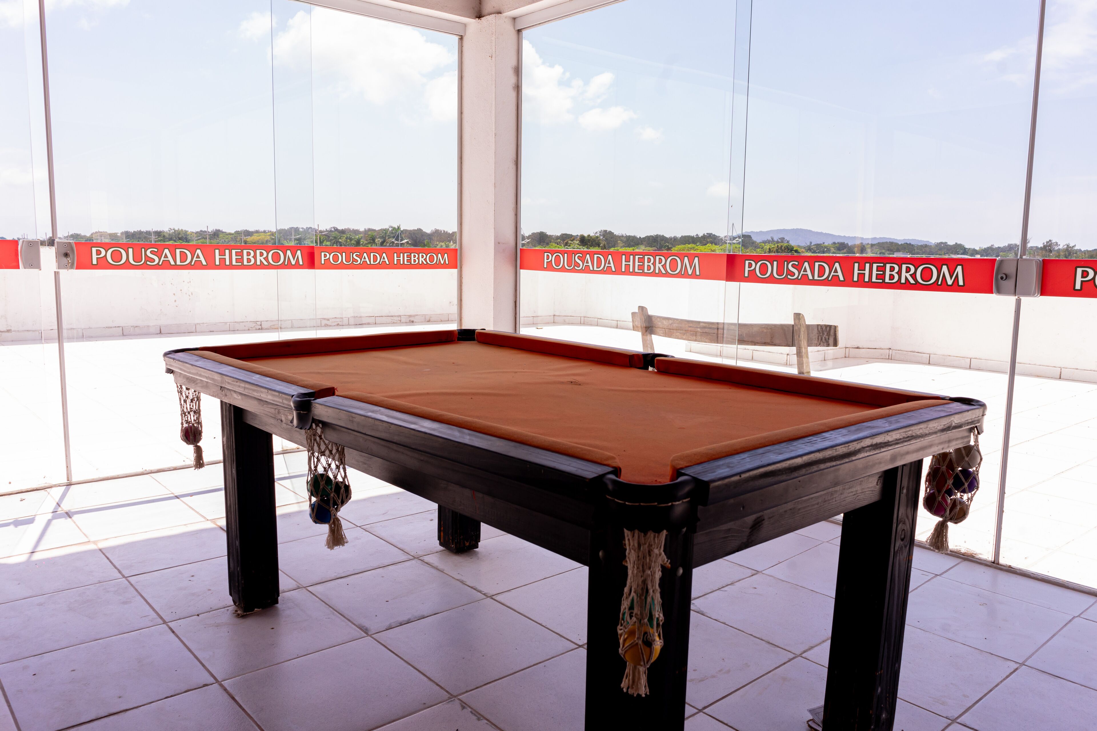 A pool table with a red felt surface, surrounded by a glass enclosure with a view of a distant landscape.