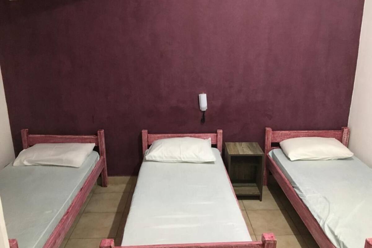A room with three single beds, each with a wooden frame and white bedding.