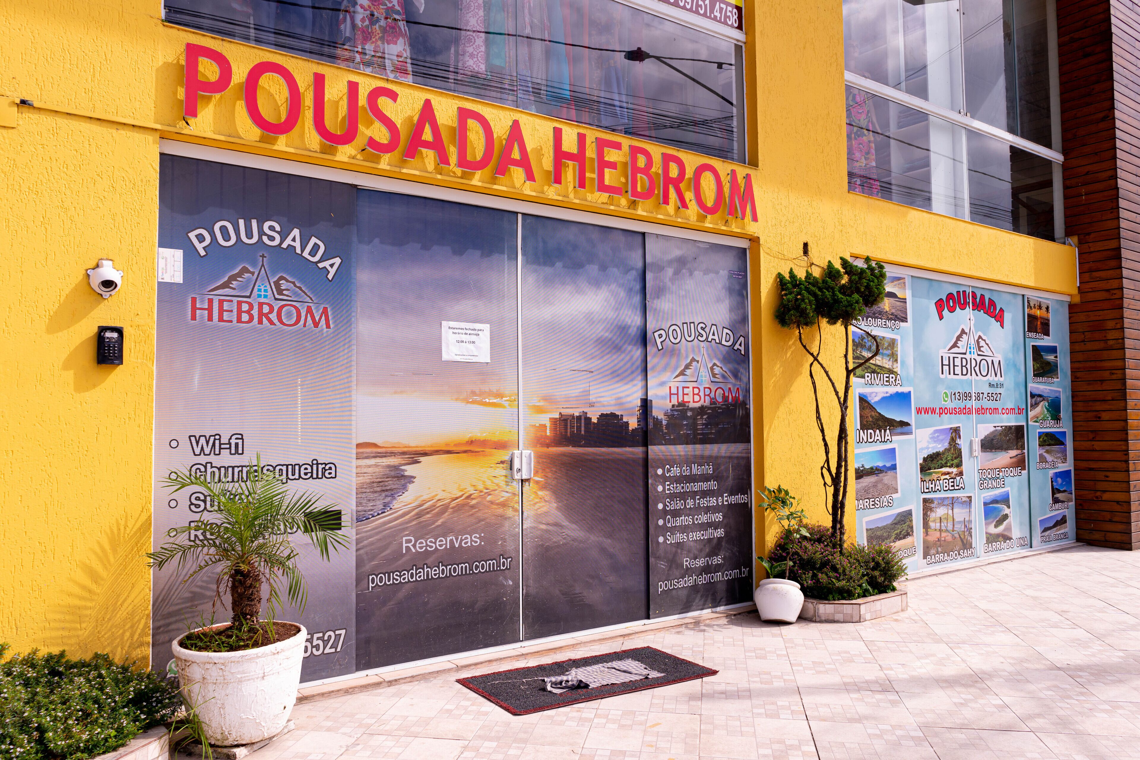 Un edificio con fachada amarilla y letreros grandes que dicen "POUSADA HEBROM".