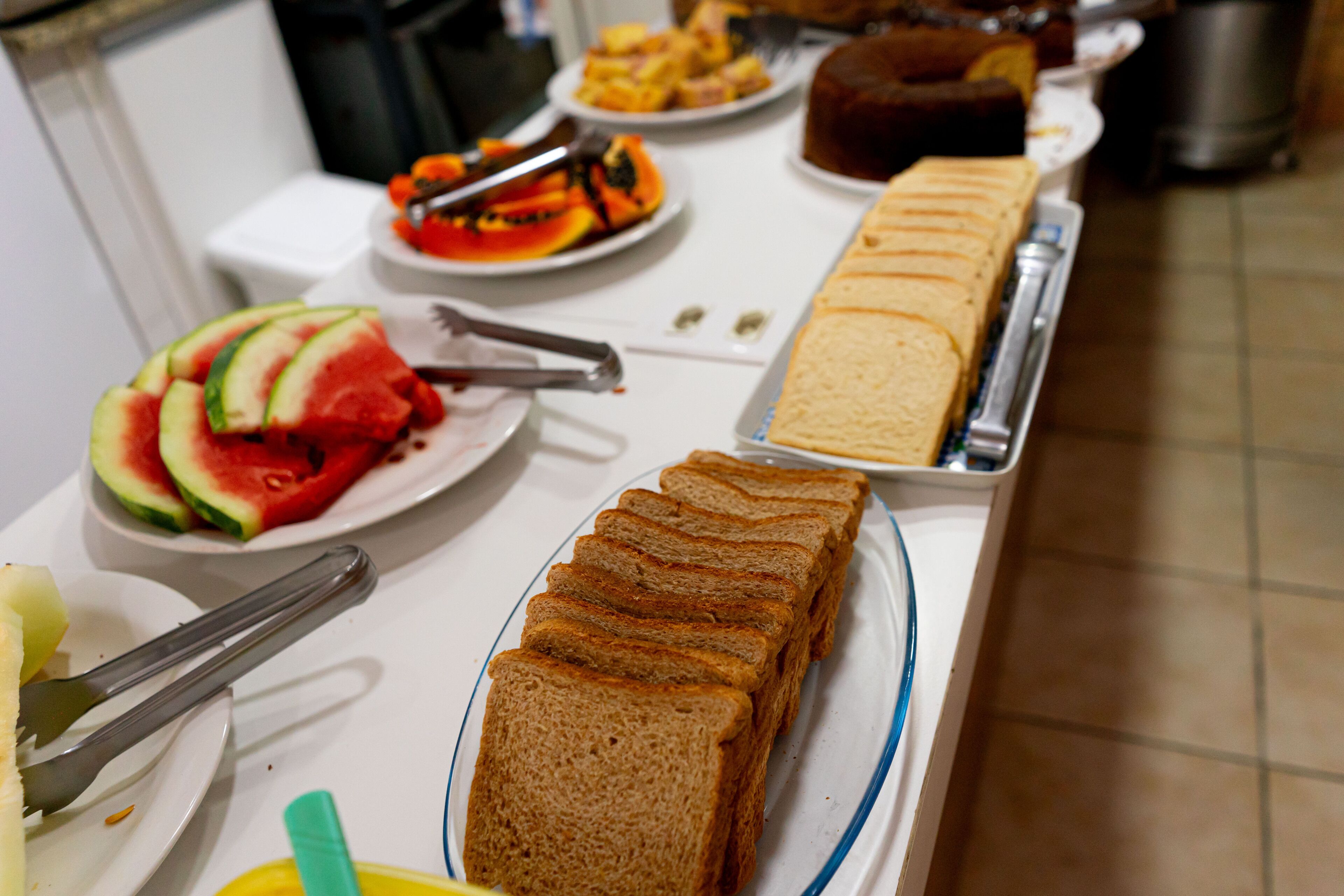 Une table de buffet proposant divers aliments, notamment des tranches de pastèque, du pain et un gâteau.