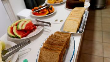 Une table de buffet proposant divers aliments, notamment des tranches de pastèque, du pain et un gâteau.