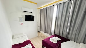 Ett hotellrum med två sängar, en TV, en luftkonditionering och ett fönster med gardiner.
