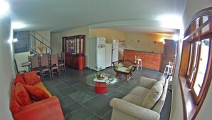 A spacious living area with a red sofa, beige sofa, and a coffee table with a red base. There is a dining area with chairs and a table, and a kitchen with a refrigerator and stove. - Plaza Morumbi (São Paulo)