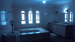 A dimly lit bathroom with a bathtub, a sink, and three windows. - Plaza Morumbi (São Paulo)
