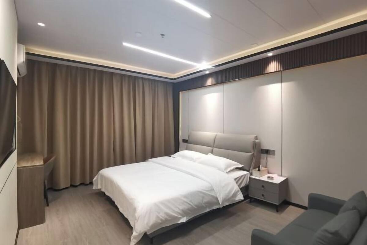 A modern hotel room with a bed, bedside table, lamp, and a large mirror.