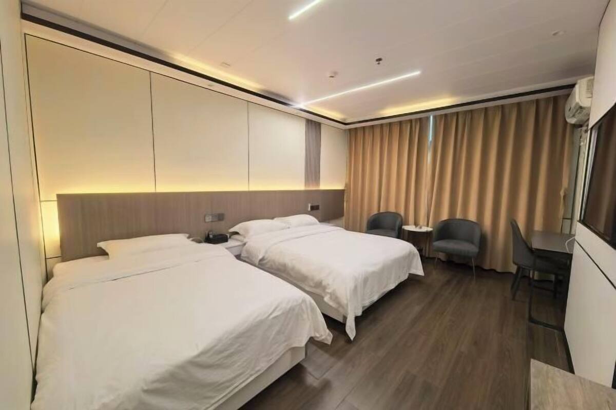 A hotel room with two beds, a desk, a chair, and a large window with curtains.