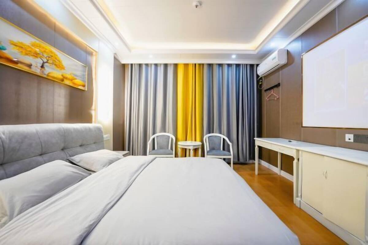 A hotel room with a bed, two chairs, a small table, a TV, and a painting on the wall.