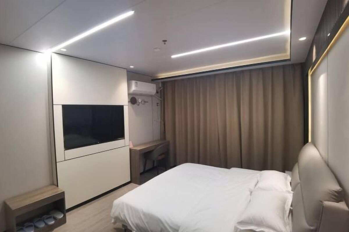 A modern hotel room with a bed, a TV, a desk, and a wardrobe.