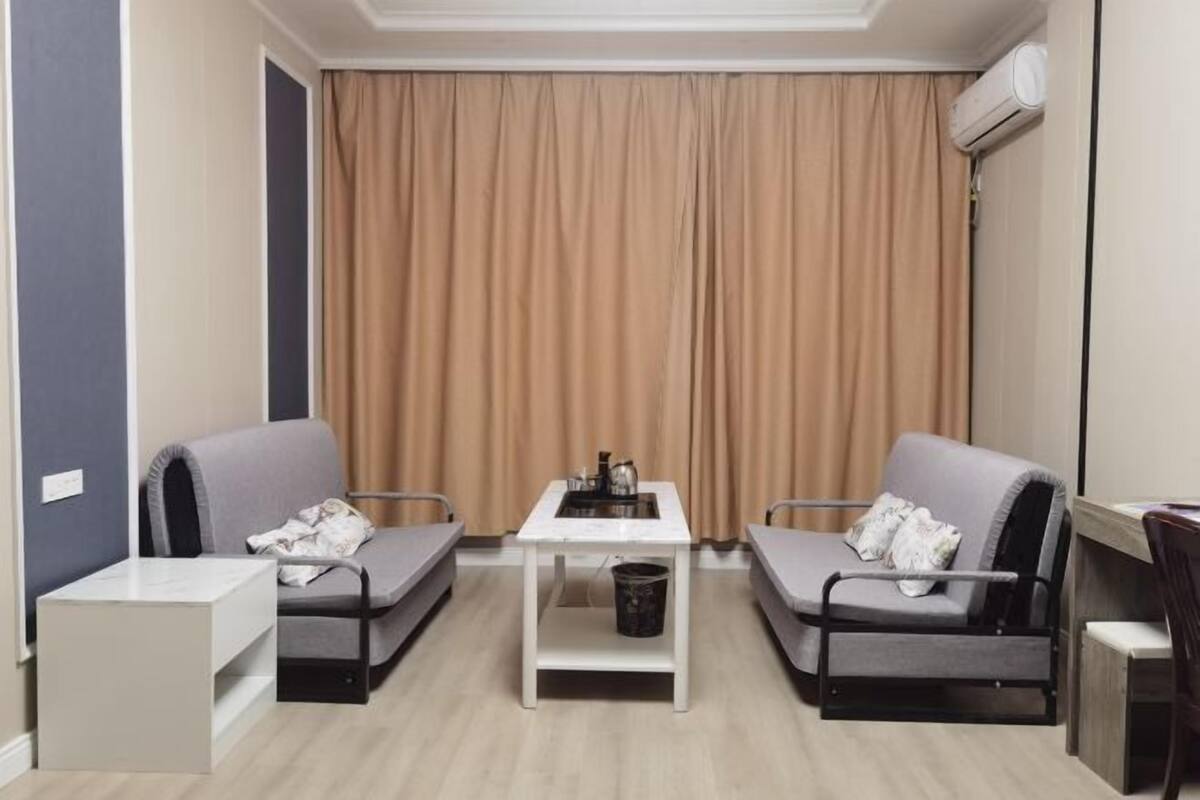 A compact room with two grey sofas, a small white table, and a beige curtain.