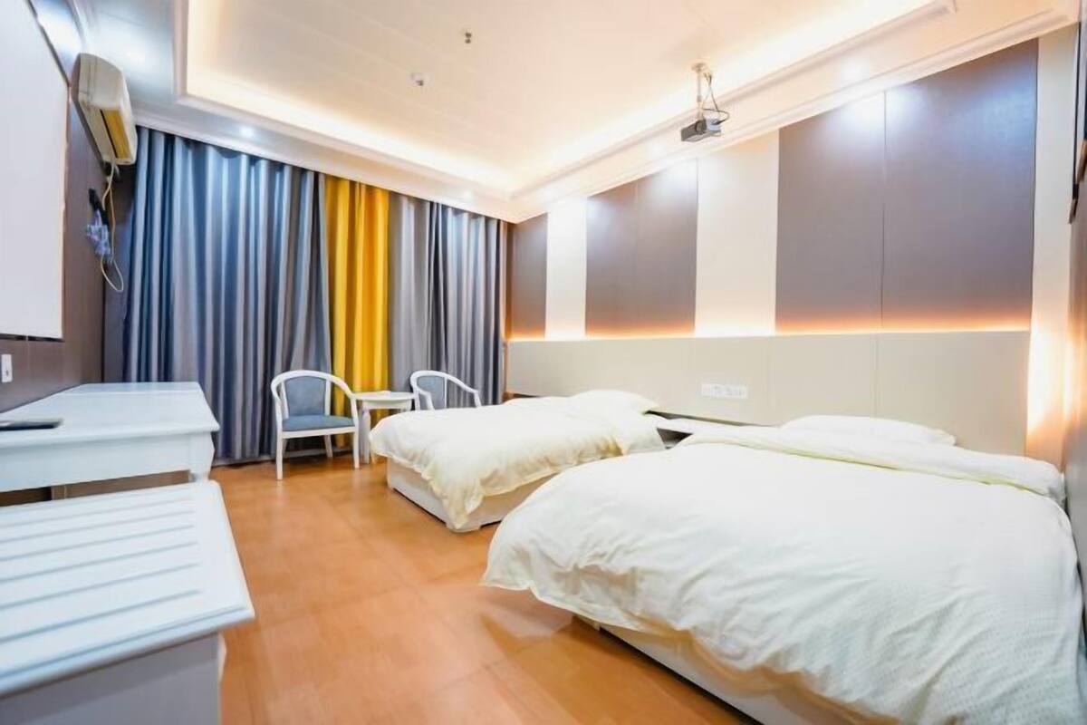 A hotel room with two beds, a desk, a chair, and a window with curtains.