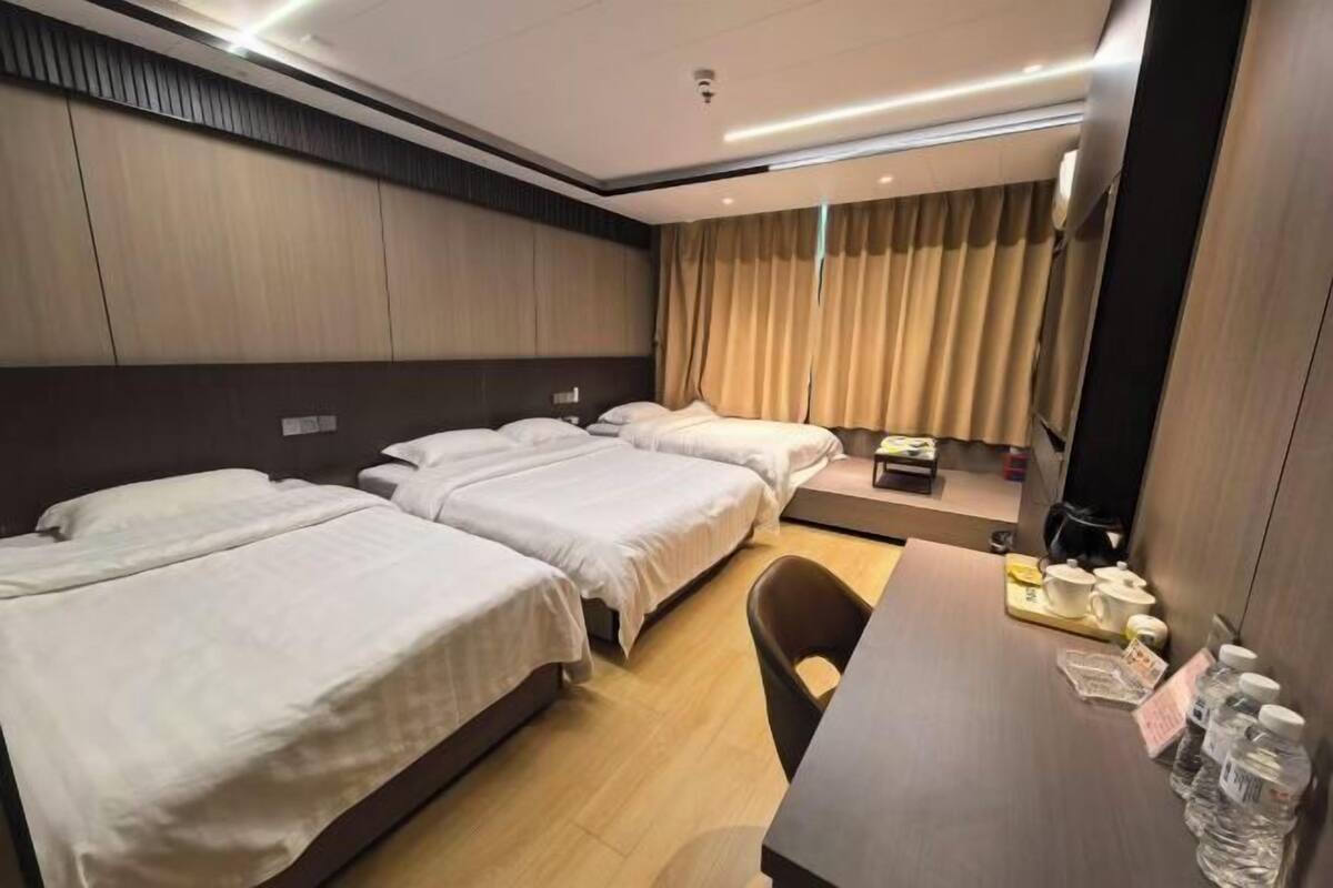 A hotel room with two beds, a desk with a chair, a small table with cups and a tray, and a window with curtains.