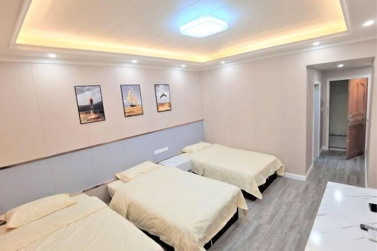 A hotel room with three single beds, a desk, and a ceiling light.