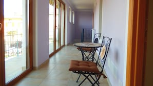 A corridor with a sliding glass door leading to a balcony, a small table with chairs, and a brown cushioned bench. - Le Colline di Maggiora (Maggiora)