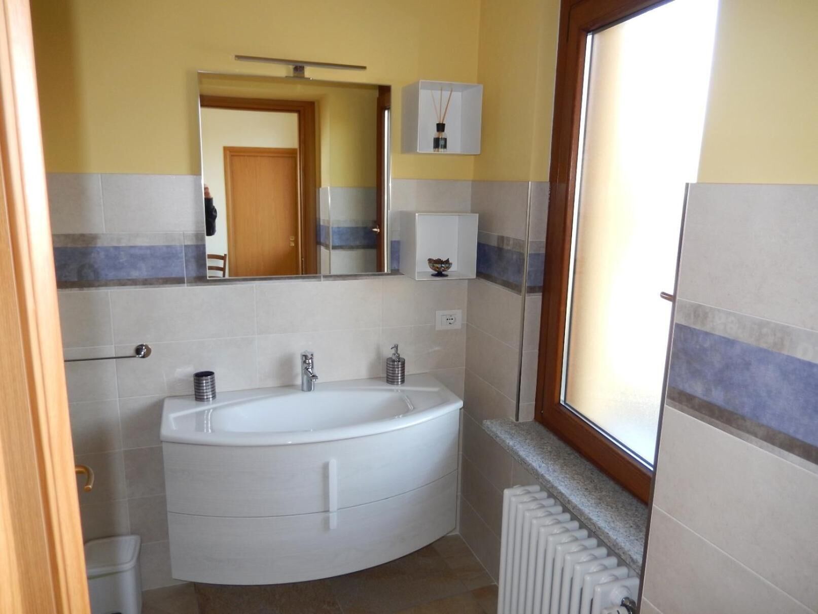 Un baño con una bañera blanca grande, un inodoro y un lavamanos. Hay un espejo sobre el lavamanos y una ventana a la derecha.