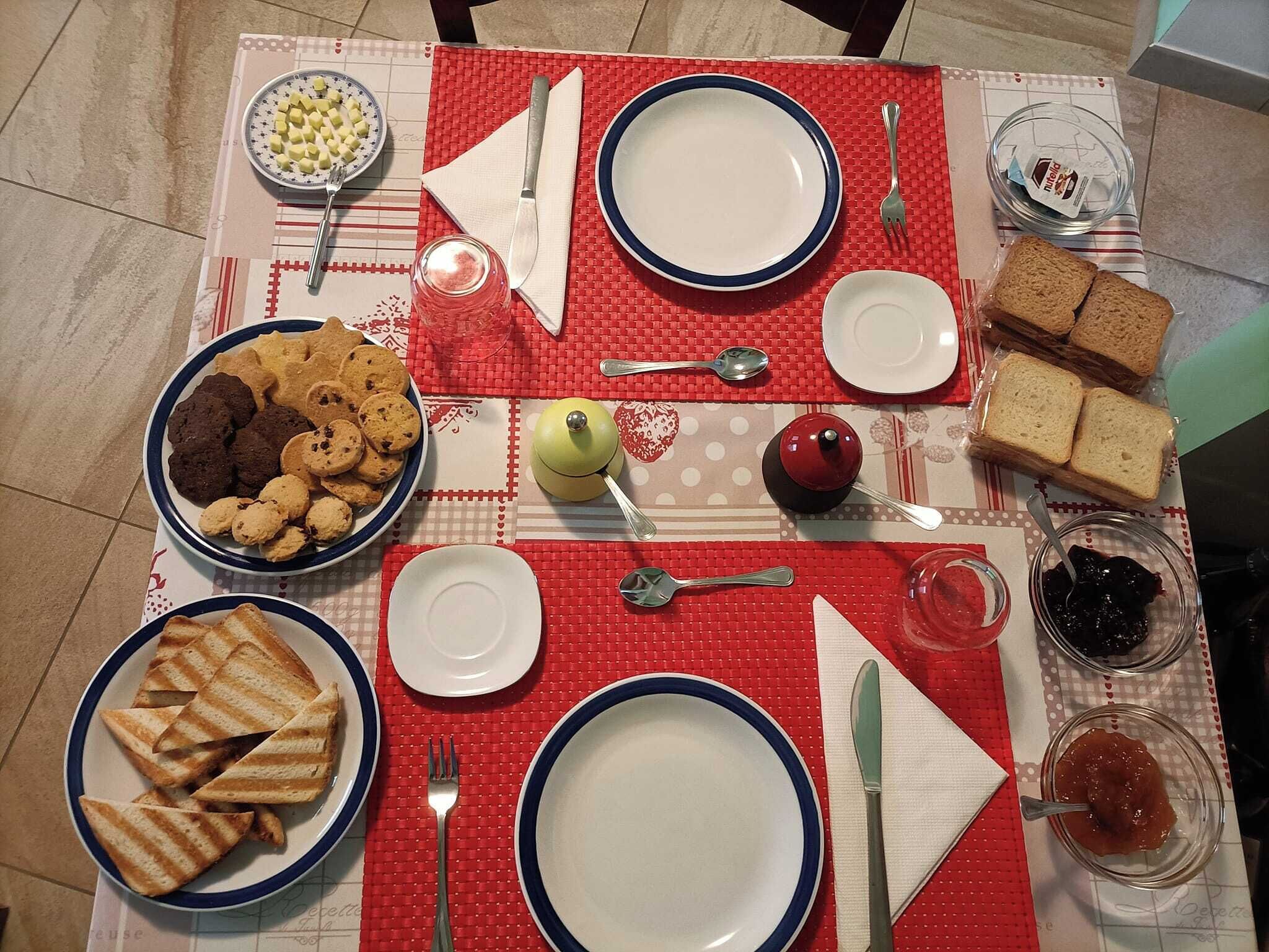A table set with plates, cutlery, cookies, jam, and bread.