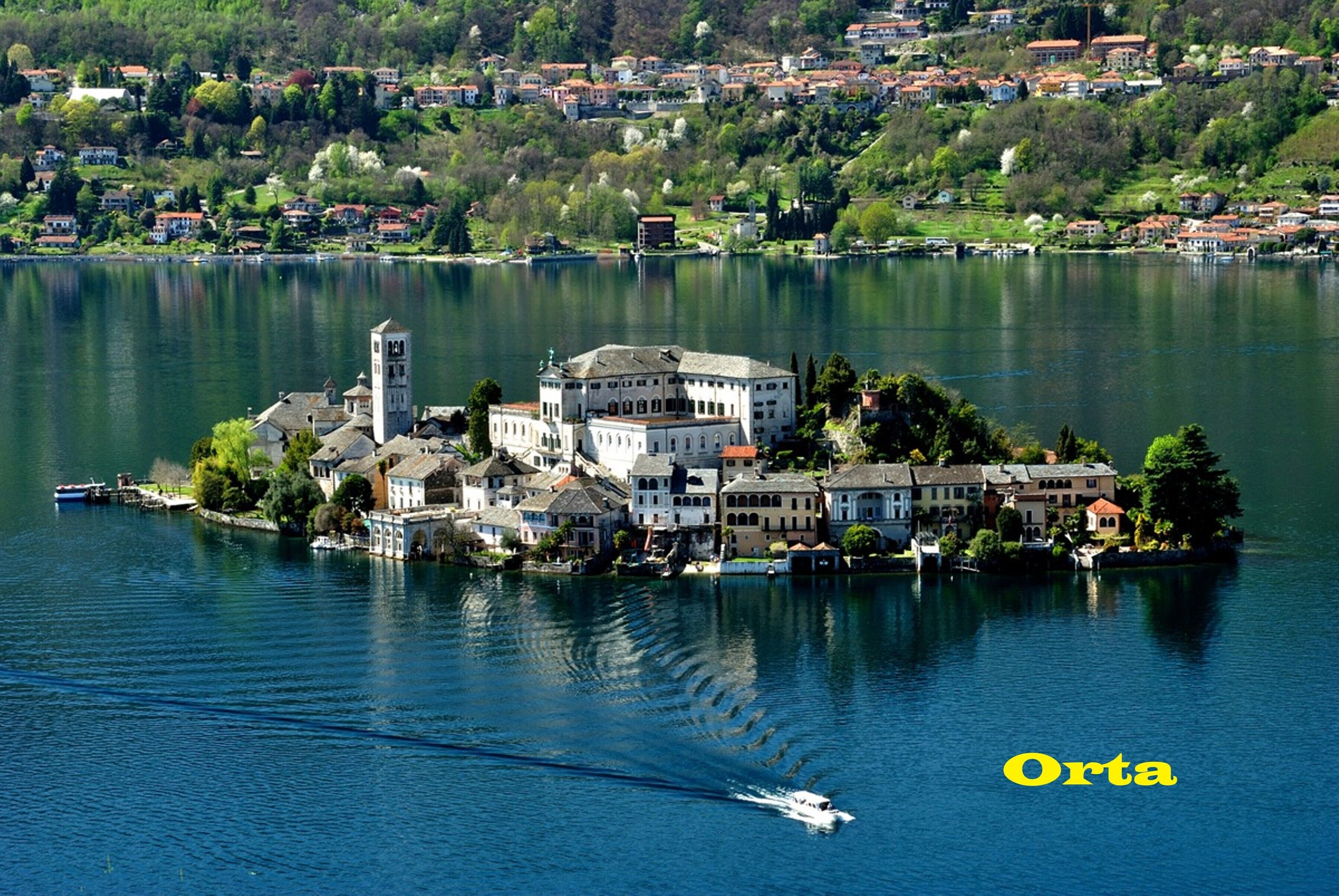 A lakeside town with a prominent white building featuring a tower, surrounded by residential houses and greenery.