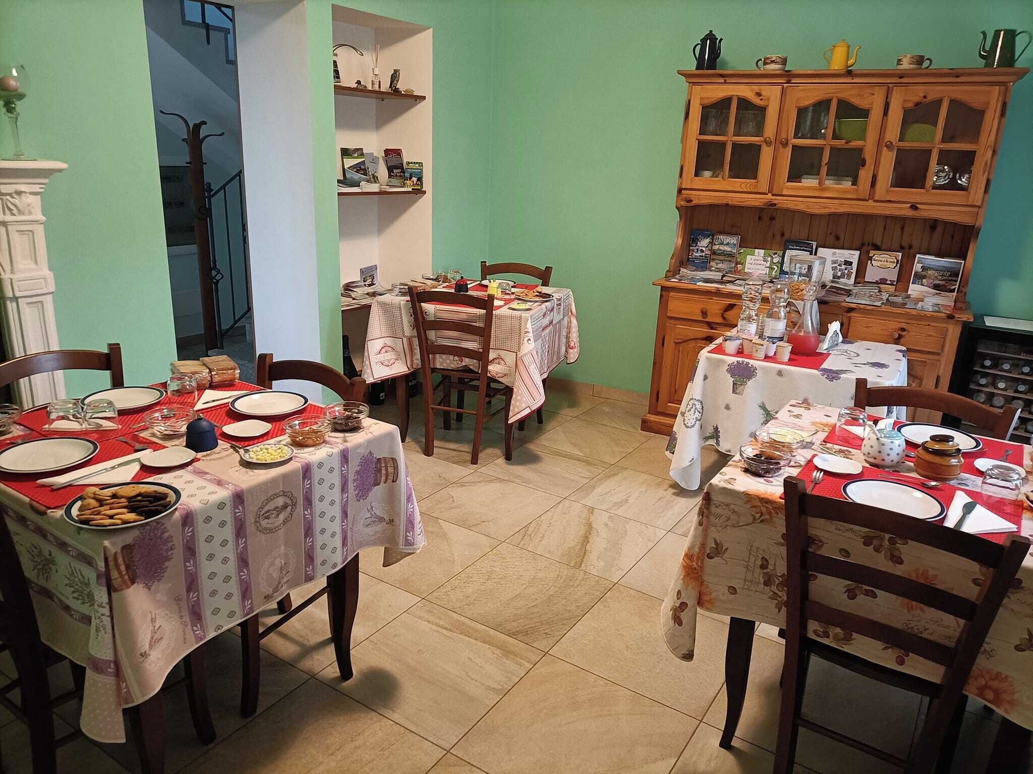 Comedor con varias mesas dispuestas para comer, sillas y un aparador de madera con puertas de cristal.