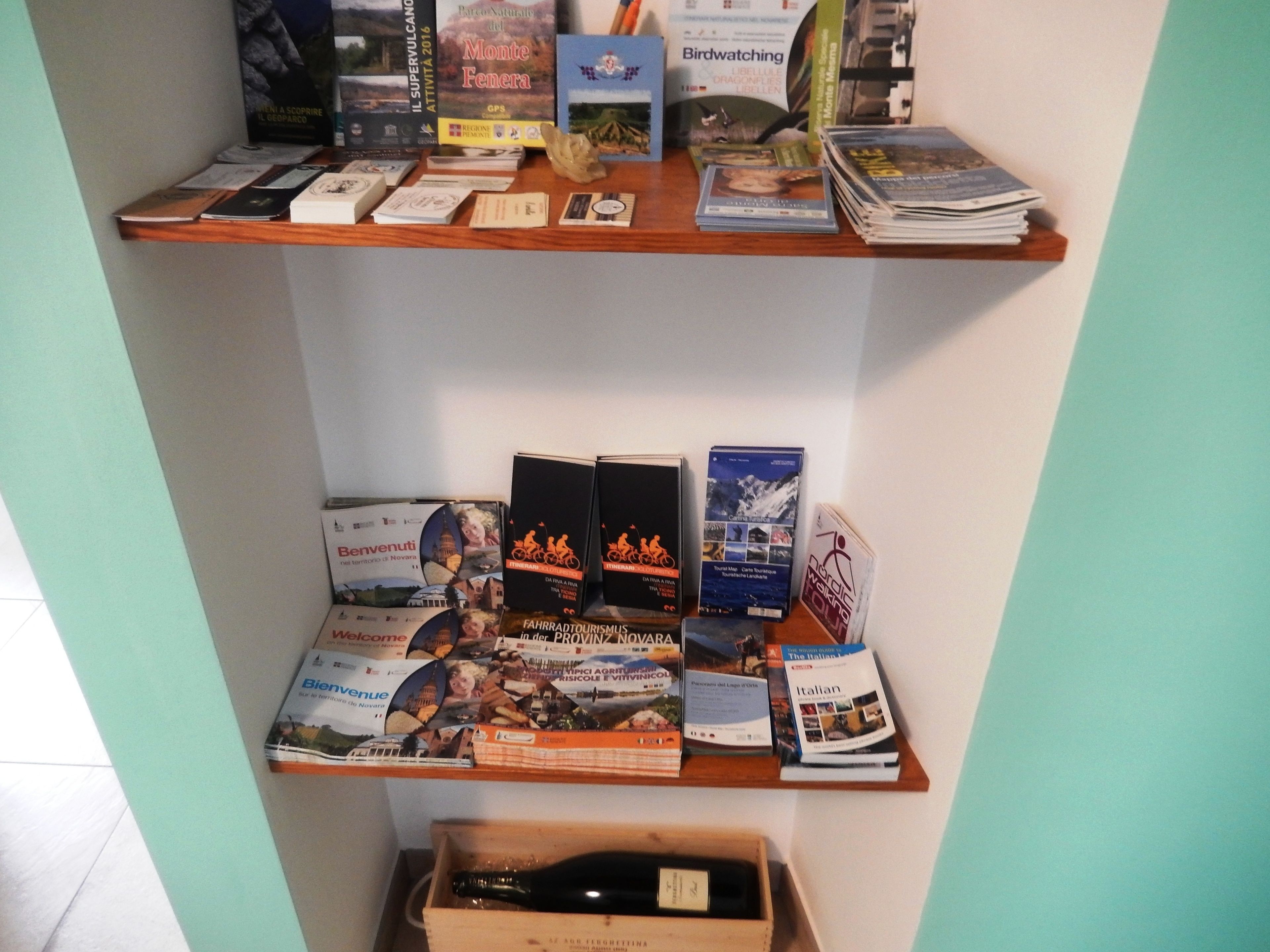 A shelf with travel brochures and a wine bottle.