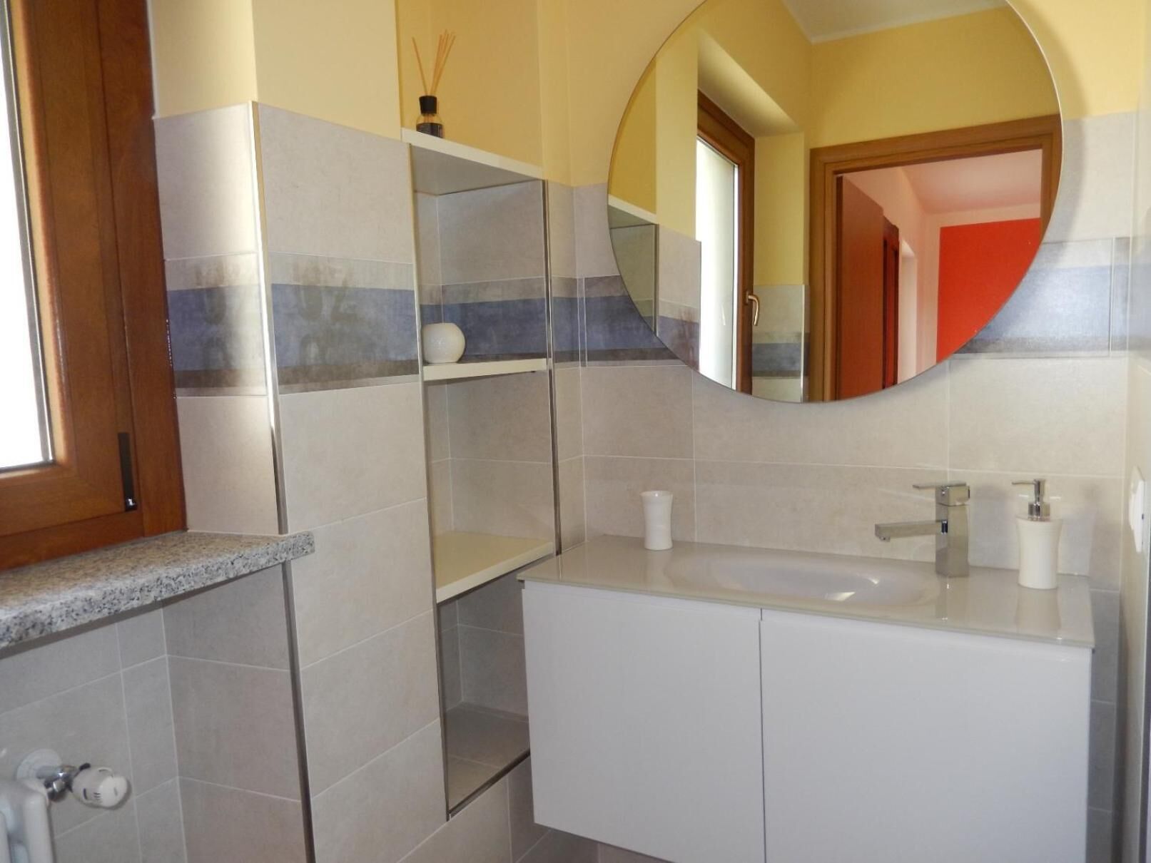 Een badkamer met een wit wastafelmeubel, een spiegel en een douchehoek.