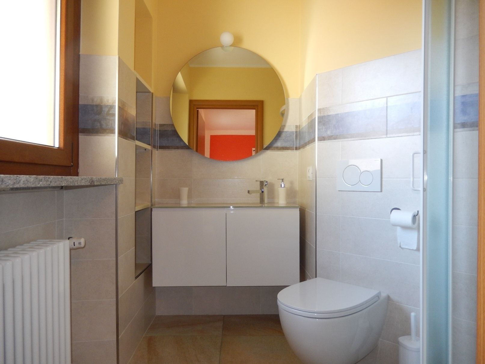 Ein kleines Badezimmer mit Toilette, Waschbecken mit Spiegel darüber und Heizkörper links.