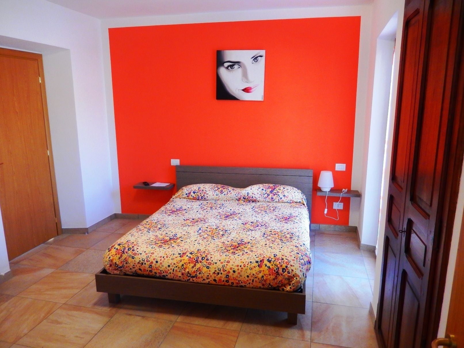 Ein Schlafzimmer mit einem Bett, einem Nachttisch, einer Lampe und einem Wandbild.
