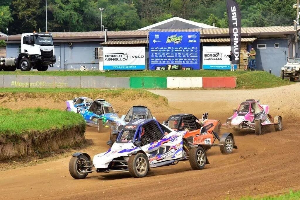 Une épreuve de rallye automobile avec plusieurs véhicules sur une piste en terre, des spectateurs en arrière-plan et une banderole publicitaire pour les sponsors.