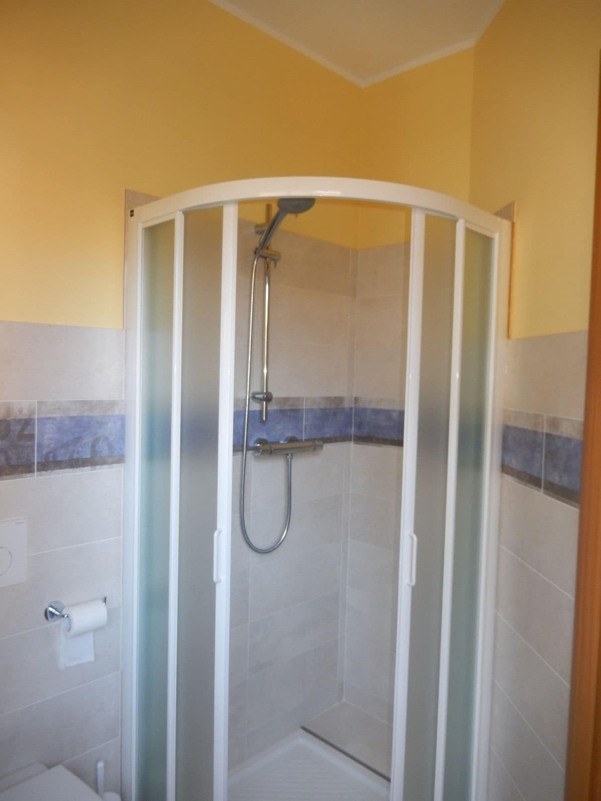 A glass-enclosed shower stall with a handheld showerhead and a wall-mounted faucet.