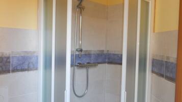 A glass-enclosed shower stall with a handheld showerhead and a wall-mounted faucet.