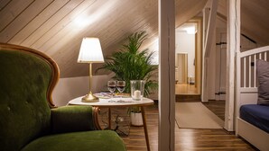 A cozy room with a green armchair, a small table with a lamp, wine glasses, and a potted plant. - ApartOne (Bautzen)